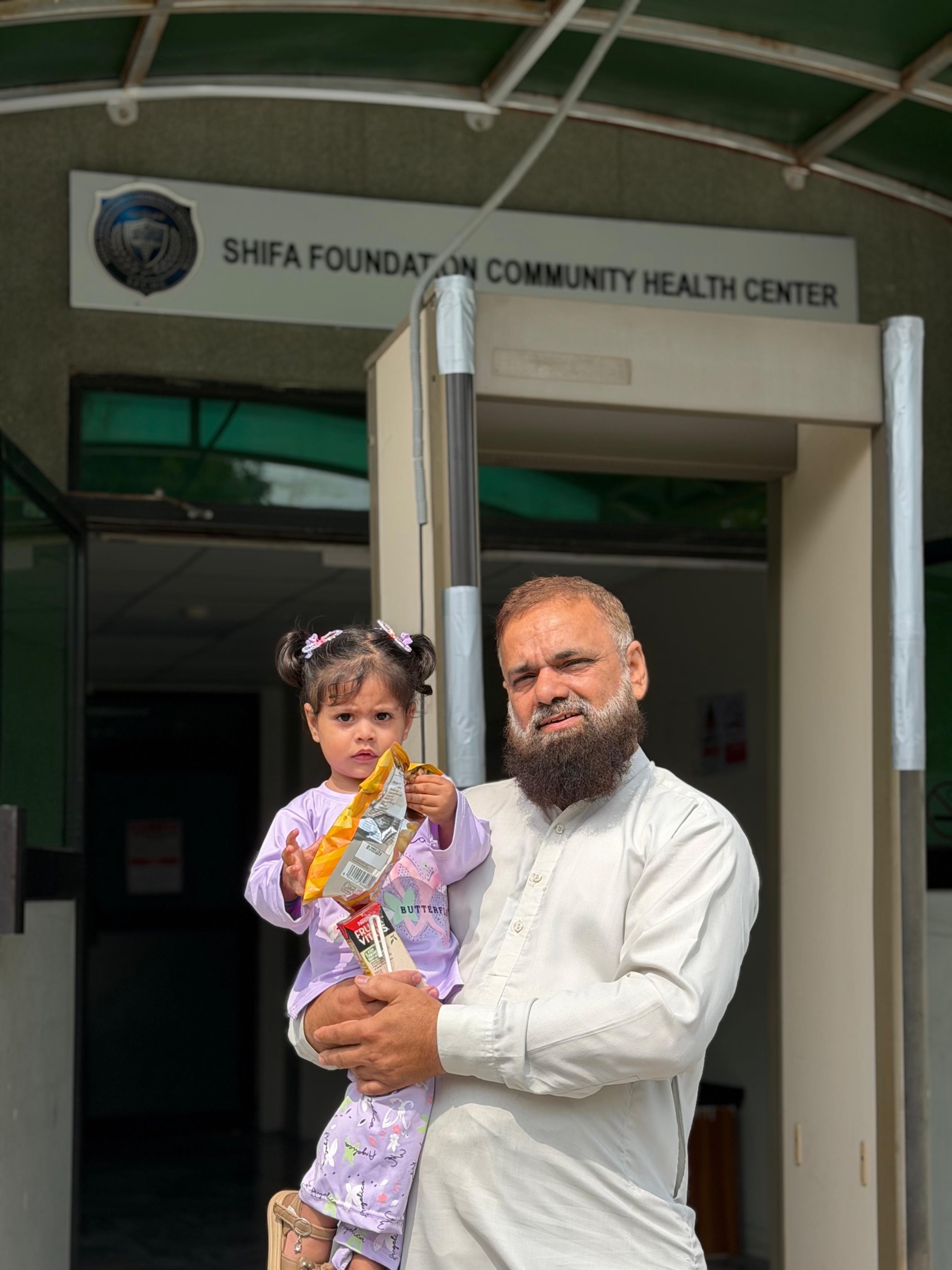 Mr. Ikramullah holding his granddaughter outside Falahi