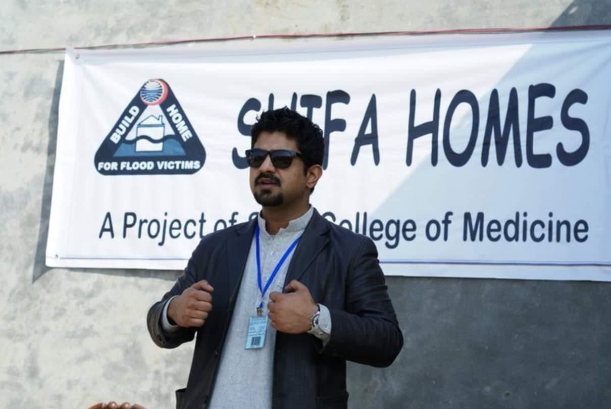 A Shifa Homes volunteer standing before the project banner